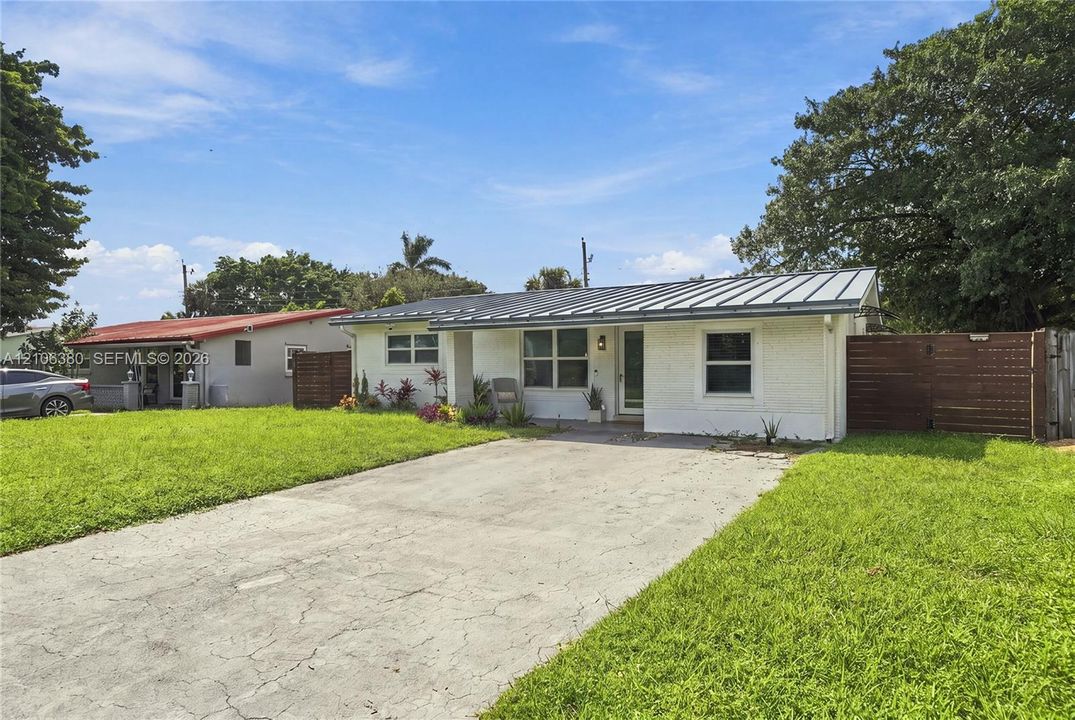 Single-story exterior featuring a painted brick facade, metal roofing, concrete driveway, and wood-slat privacy fencing