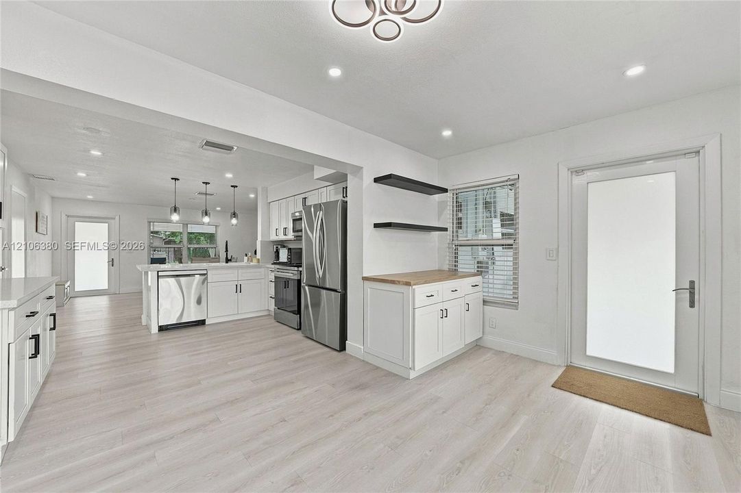 Kitchen featuring white cabinetry, stainless steel appliances, wood-finish flooring, recessed lighting, and a butcher-block countertop workspace with floating shelving