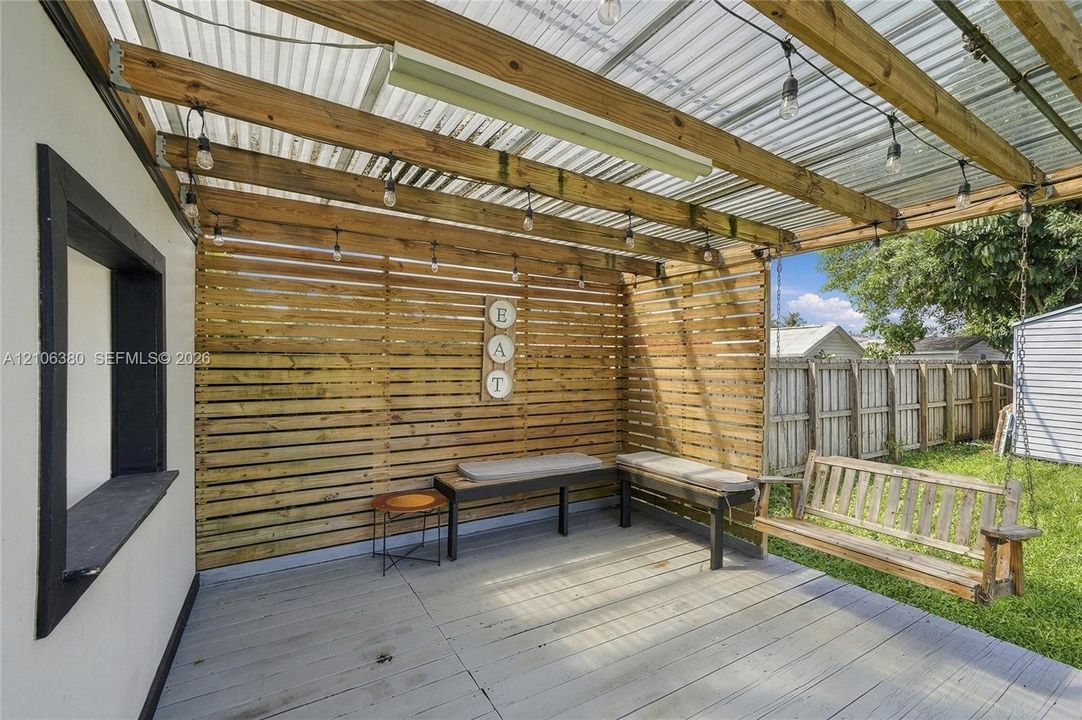 Covered patio featuring a corrugated translucent roof, horizontal wood-slat privacy screen, painted wood decking, and built-in string lighting