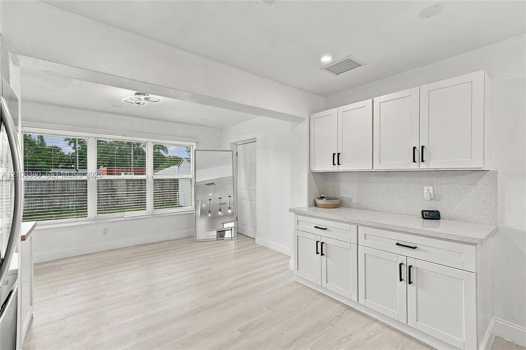 White cabinetry with matte black hardware, stone-finish countertops, light wood-finish flooring, and multi-pane windows