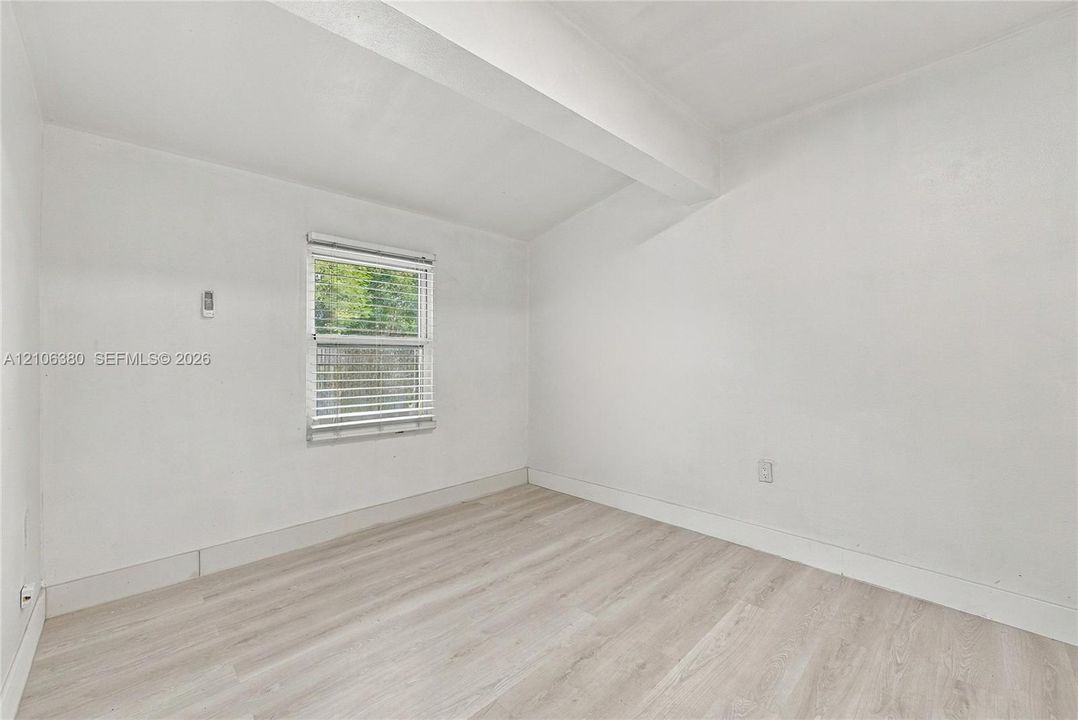 Interior room featuring wood-finish flooring, a single-pane window with adjustable blinds, and smooth-finish walls