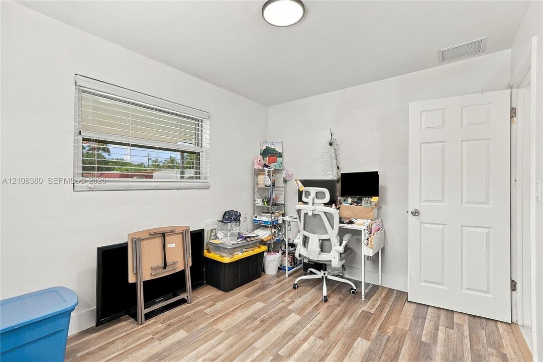 Room featuring wood-finish flooring, a horizontal sliding window with blinds, a six-panel door, and a flush-mount ceiling light