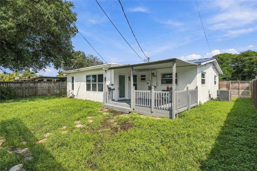Rear exterior featuring a covered wood deck with railing, stucco siding, and a fenced backyard