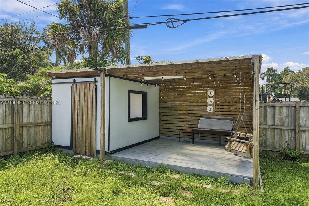 Detached structure featuring a covered wood-decked patio, horizontal wood slat privacy wall, sliding barn-style door, and attached overhead string lighting