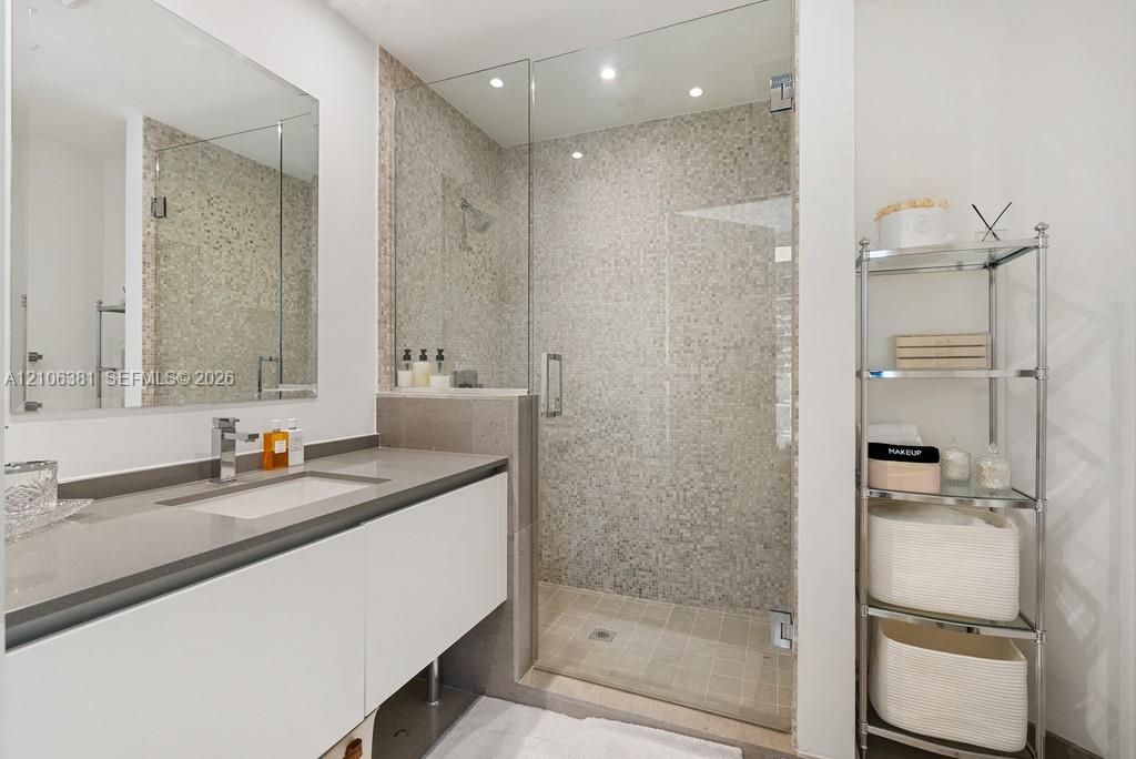 Modern floating vanity with a solid-surface countertop and integrated sink, frameless glass walk-in shower with textured tile surround, and expansive wall-mounted mirror