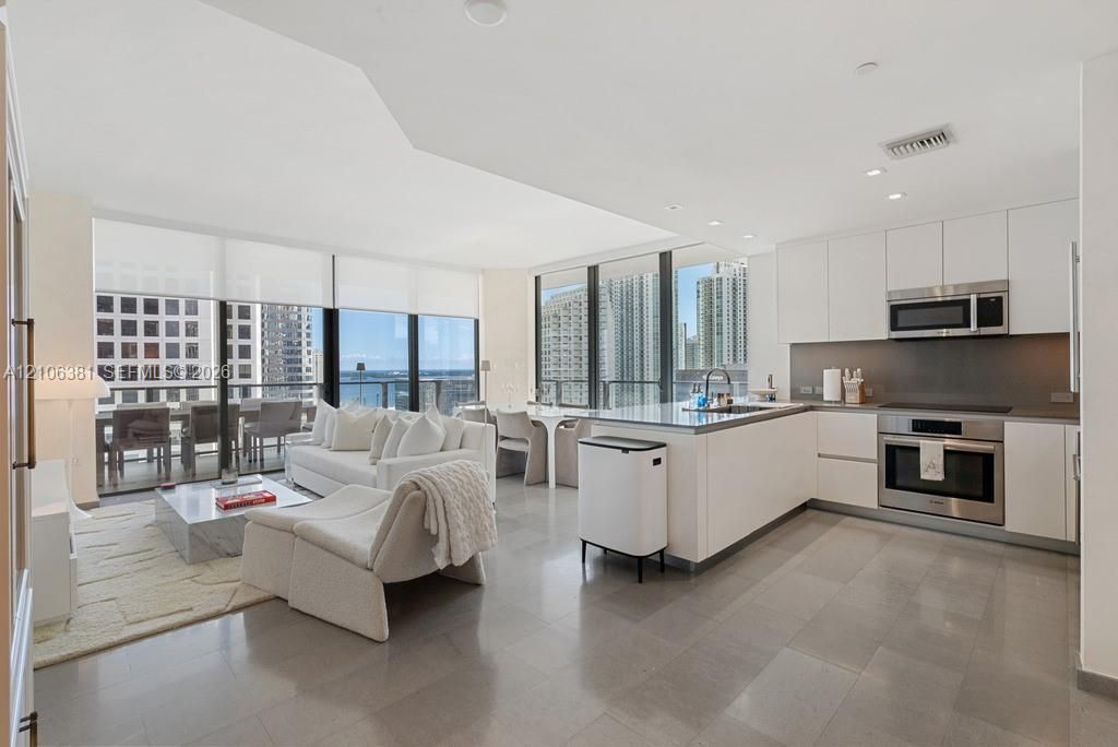 Open-concept kitchen featuring flat-panel cabinetry, stainless steel appliances, and stone countertops, complemented by floor-to-ceiling windows and tile flooring