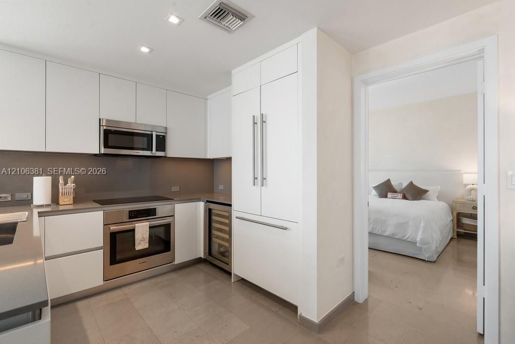 Modern kitchen featuring flat-panel white cabinetry, solid-surface countertops, integrated stainless steel appliances, built-in wine cooler, and recessed lighting