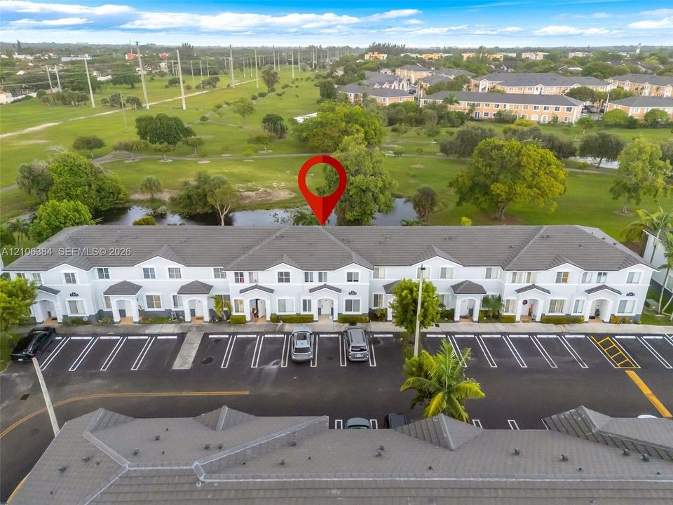 Multi-unit residential complex featuring a concrete tile roof, light-toned stucco exterior, dedicated surface parking, and perimeter pond frontage