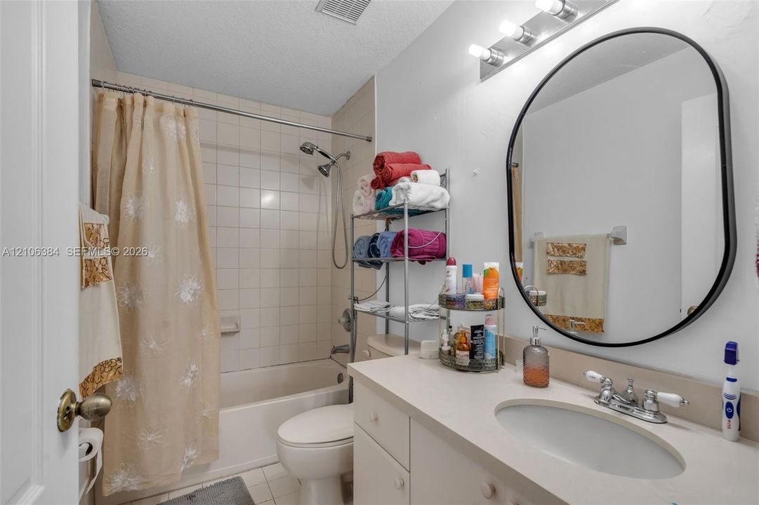 Bathroom featuring a vanity with integrated sink, oval wall-mounted mirror, three-light fixture, and a tiled shower-tub combination