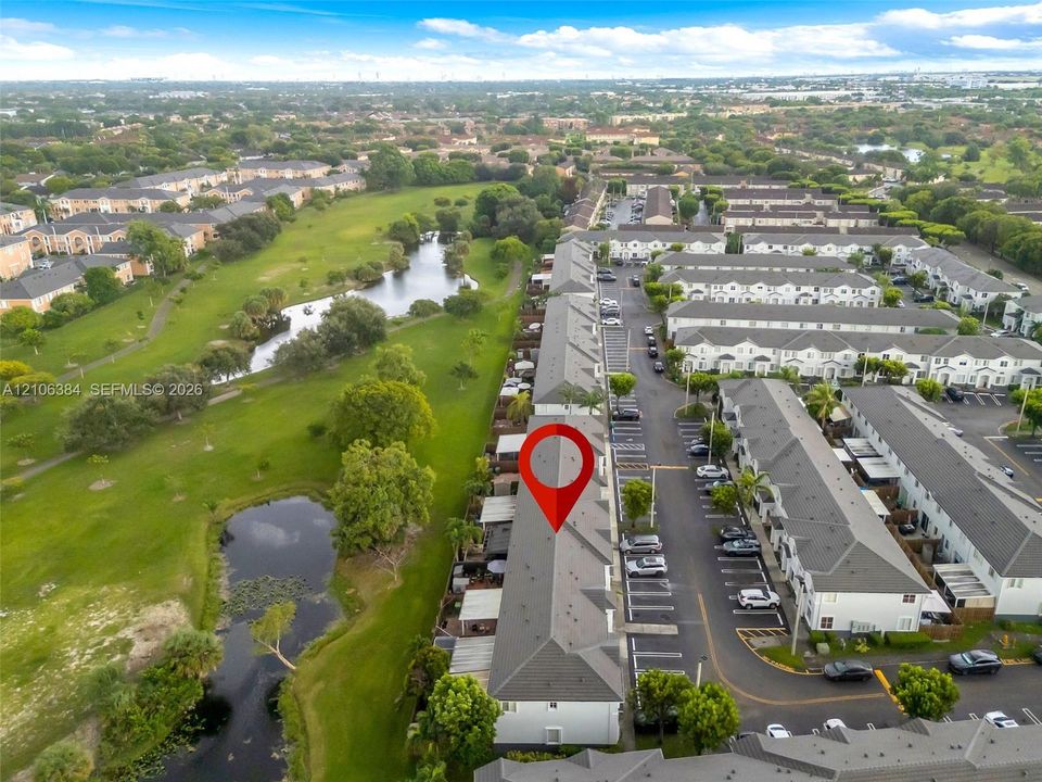 Aerial perspective of multi-story townhome community featuring asphalt shingle roofing, paved surface parking, and exterior green space