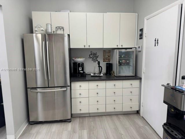 Custom cabinetry featuring white flat-panel doors, dark stone-finish countertops, stainless steel French-door refrigerator, and wood-finish flooring