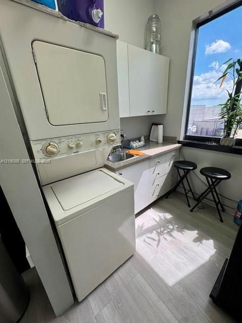 Laundry area featuring a stacked washer and dryer, solid surface countertop, inset stainless steel sink, white cabinetry, and wood-finish flooring