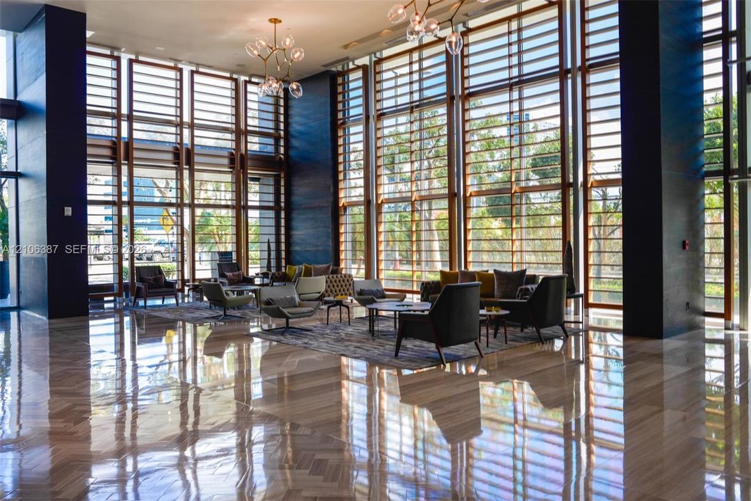 Double-height floor-to-ceiling windows with wood-tone mullions, polished stone flooring, and contemporary multi-arm pendant lighting