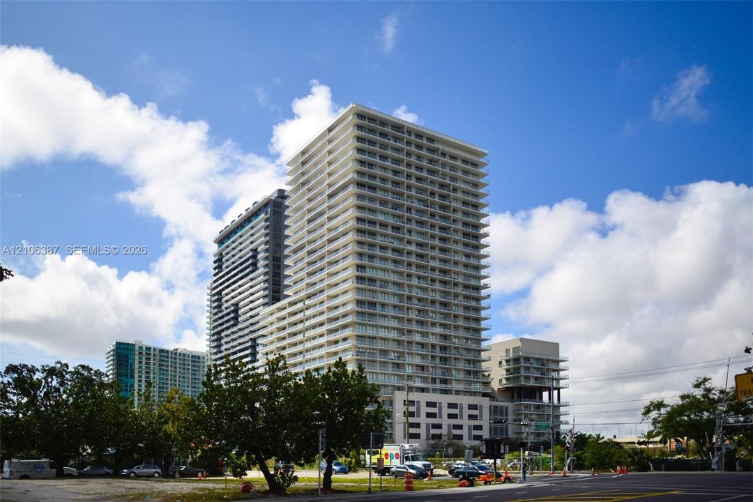 High-rise residential tower featuring a concrete facade, tiered floor levels, glass balcony railings, and a multi-story podium structure