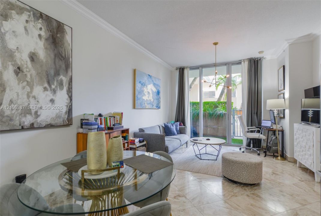 Polished stone flooring, crown molding, multi-arm chandelier, and expansive floor-to-ceiling glass sliding doors opening to a private outdoor space