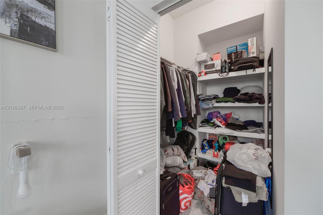 Storage closet featuring white louvered doors and built-in shelving