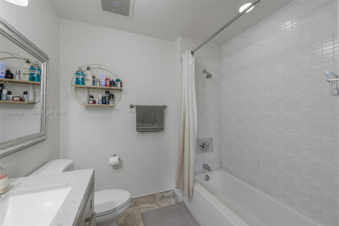 Bathroom featuring a vanity with a light-toned countertop, a shower-tub combination with white tile surround, and a metal towel bar
