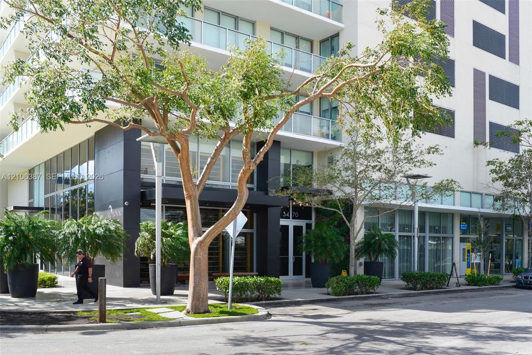 Multi-story exterior facade featuring floor-to-ceiling glass windows, glass-panel balcony railings, black paneling accents, and exterior hardscaping