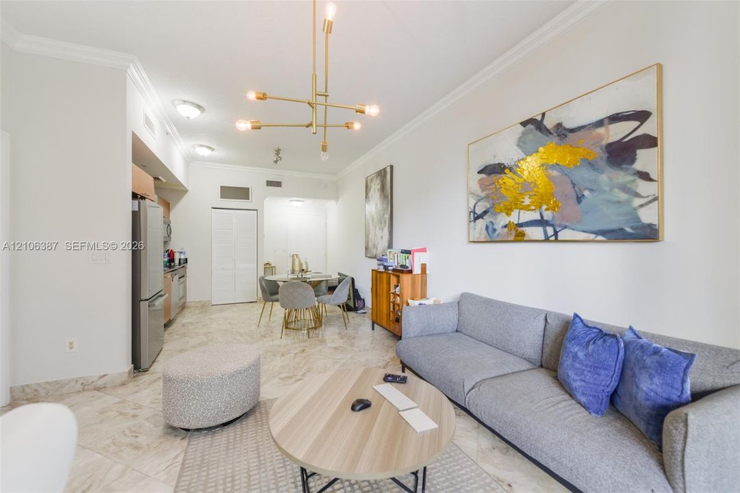Open-concept space featuring polished stone flooring, crown molding, modern multi-arm brass chandelier, and built-in stainless steel appliances