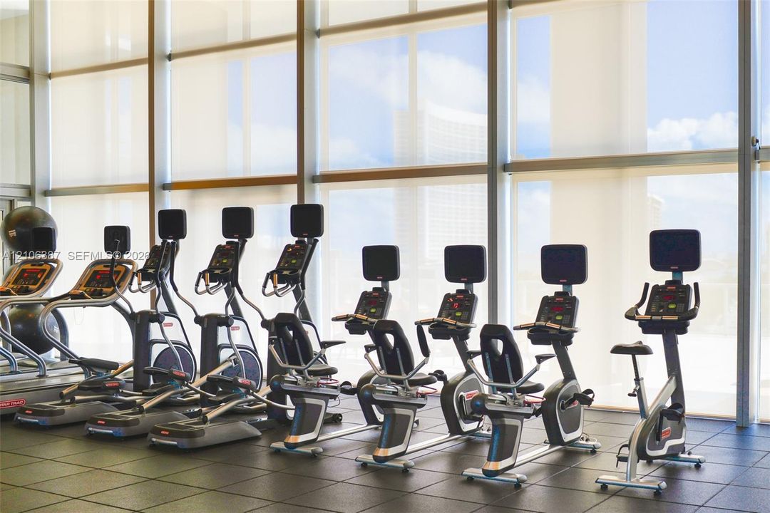 Fitness center featuring floor-to-ceiling windows with metal framing, motorized solar shades, and industrial-grade rubber flooring