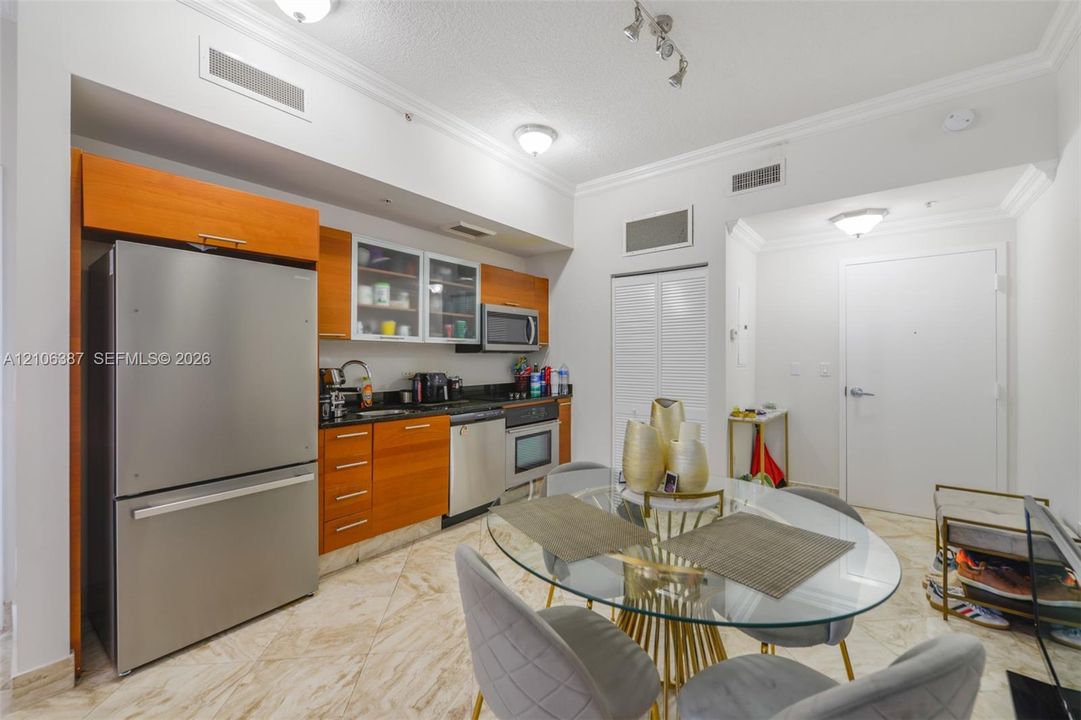 Kitchen featuring wood-veneer cabinetry, stainless steel appliances, glass-front upper cabinets, dark solid-surface countertops, and diagonal-patterned stone flooring