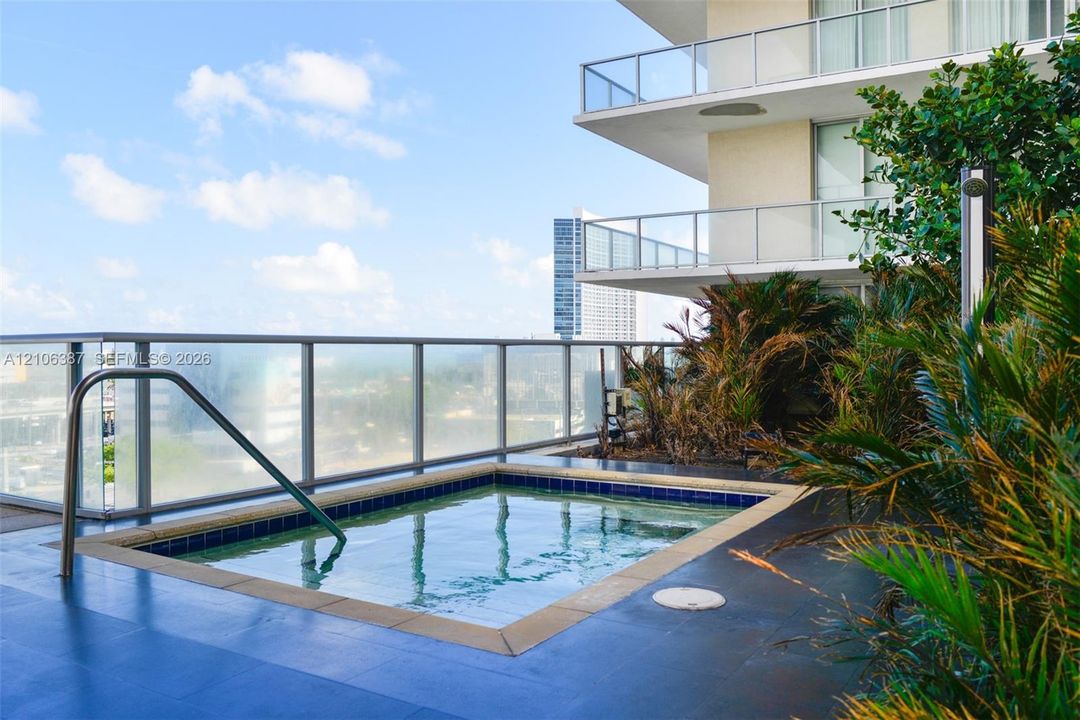 Outdoor terrace featuring an in-ground spa, tile surround, glass railing, and integrated landscaping