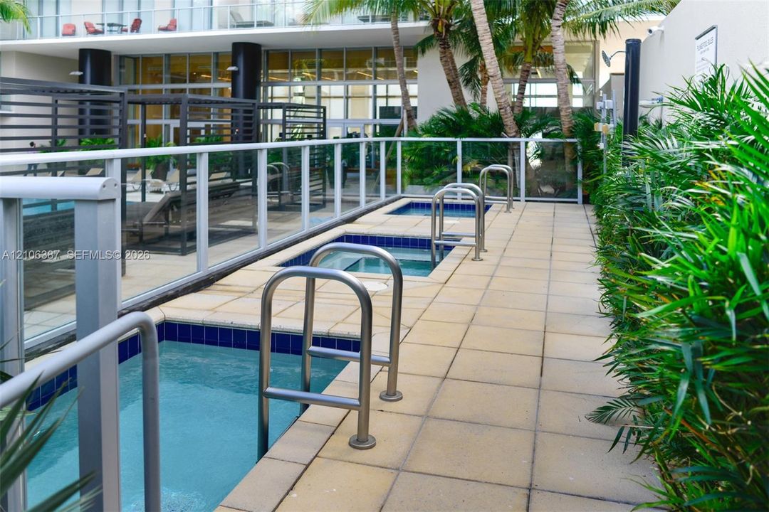Terrace level featuring multiple in-ground spa basins, large-format paver decking, metal perimeter fencing, and established palm landscaping