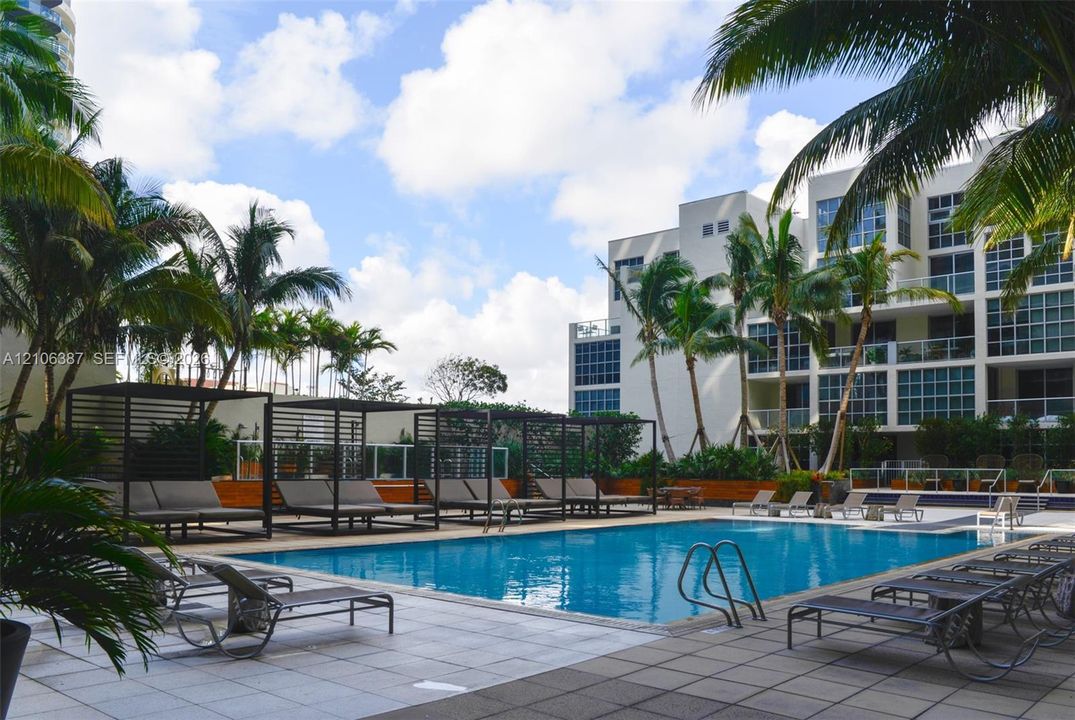 Swimming pool with surrounding tiled deck, structured metal cabanas, and mature palm trees