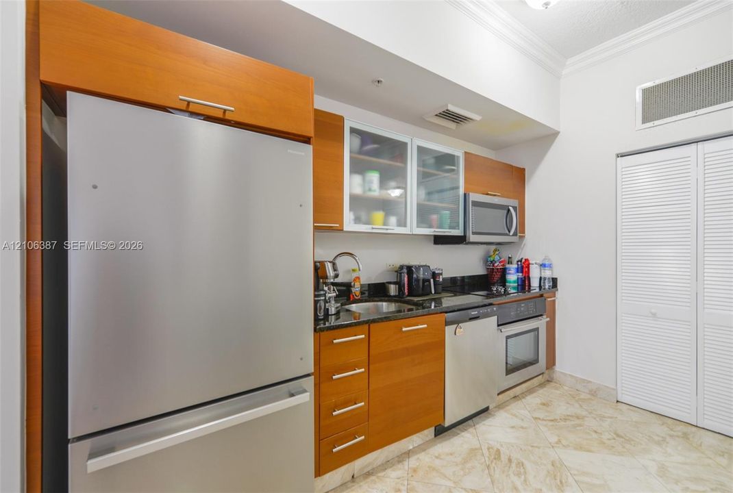 Kitchen featuring wood cabinetry, stone countertops, stainless steel appliances, glass-front upper cabinets, and tile flooring