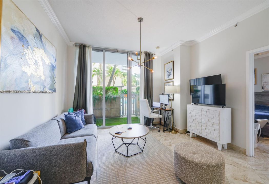 Floor-to-ceiling glass sliding doors, stone-finish flooring, crown molding, and a modern multi-arm light fixture