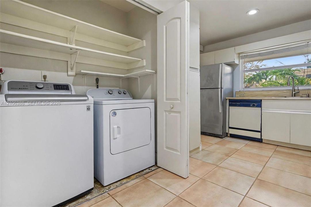 Laundry area featuring open wall-mounted shelving and tile flooring, with built-in cabinetry, stainless steel refrigerator, and integrated dishwasher