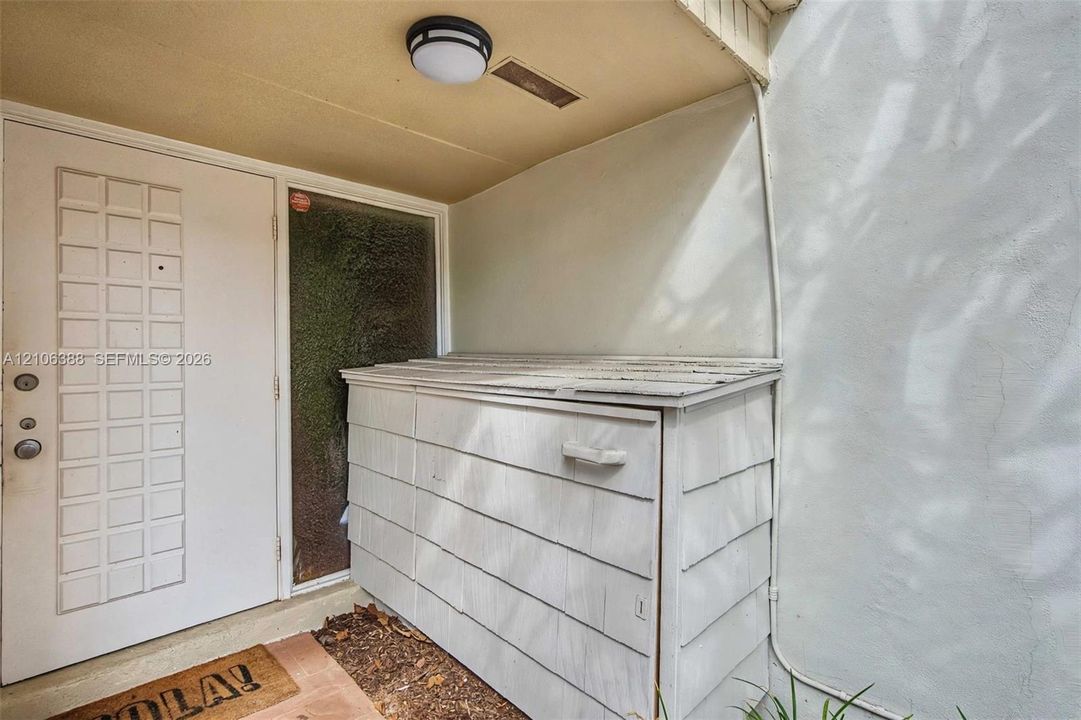 Entryway featuring a solid door with decorative recessed panels, a textured glass sidelight, exterior shiplap-style storage unit, and a flush-mount circular ceiling fixture