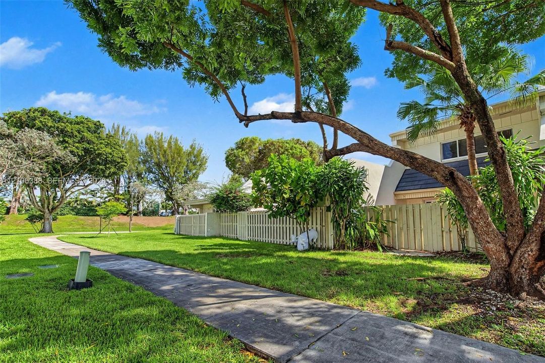 Manicured lawn featuring mature shade trees, a concrete pathway, and perimeter wood privacy fencing