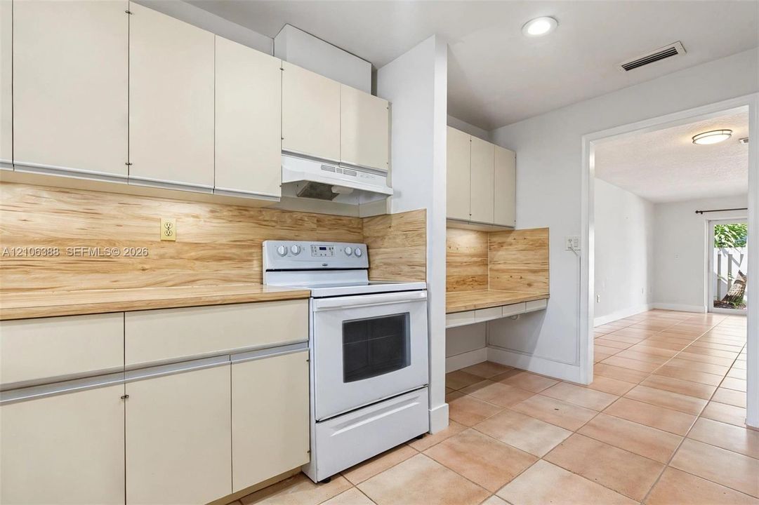 Kitchen featuring flat-panel cabinetry, light-toned wood-finish backsplash, integrated range hood, tile flooring, and built-in workstation