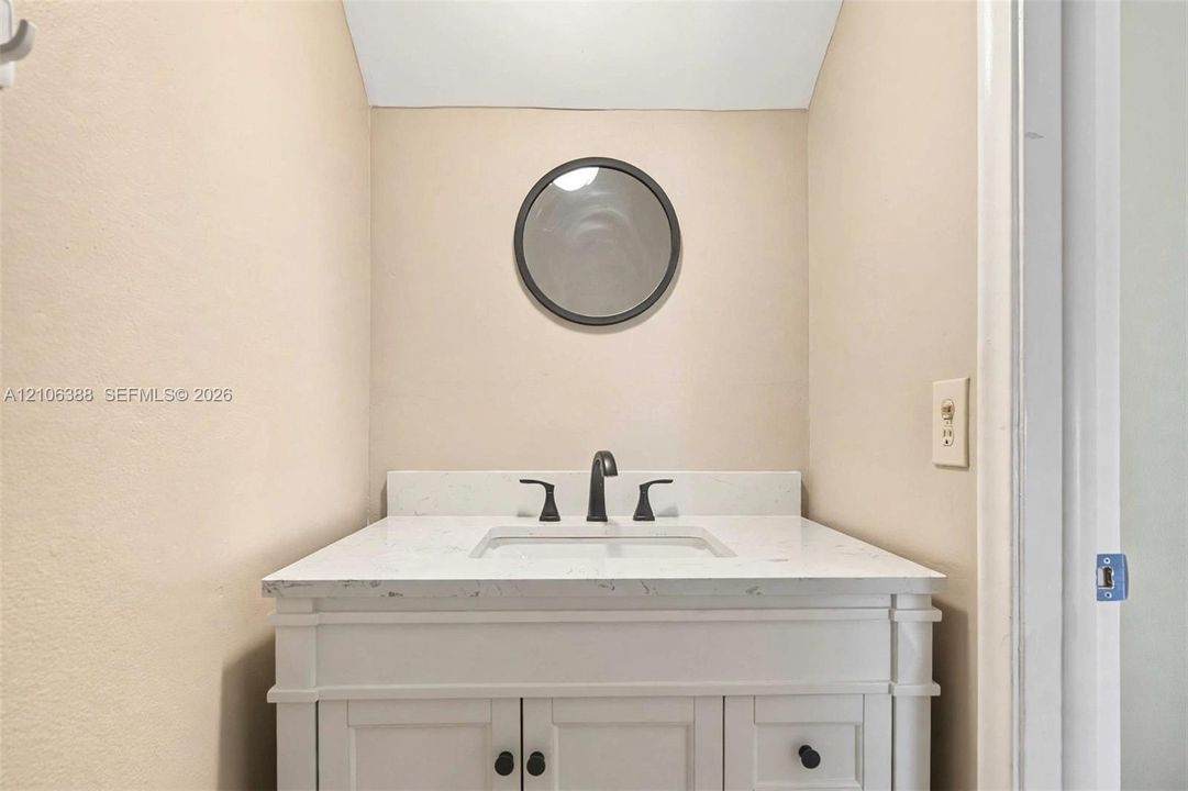 White vanity featuring a stone-surface countertop, an integrated rectangular sink, matte black widespread faucet hardware, and a circular mirror with a dark frame