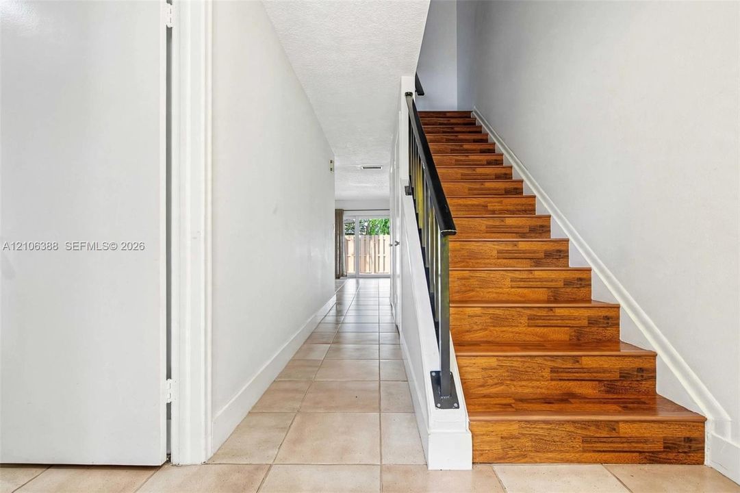 Entryway featuring square ceramic floor tiling, staircase with wood-finish treads, and a matte black metal handrail