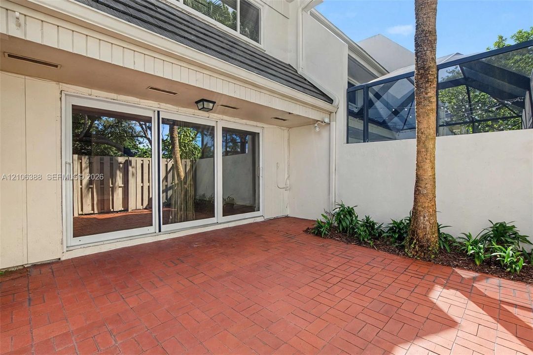 Private courtyard featuring brick paver flooring, sliding glass doors, a screened-in enclosure, and mature palm landscaping