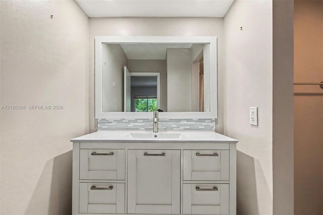 White cabinetry vanity featuring a rectangular integrated sink, white countertop, linear tile backsplash, and a framed mirror