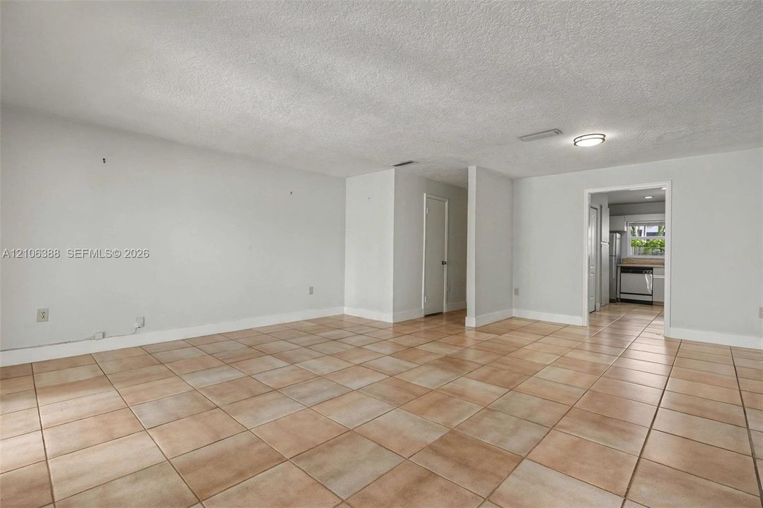 Neutral-toned interior space featuring light-colored ceramic tile flooring, a textured ceiling, and a flush-mount light fixture
