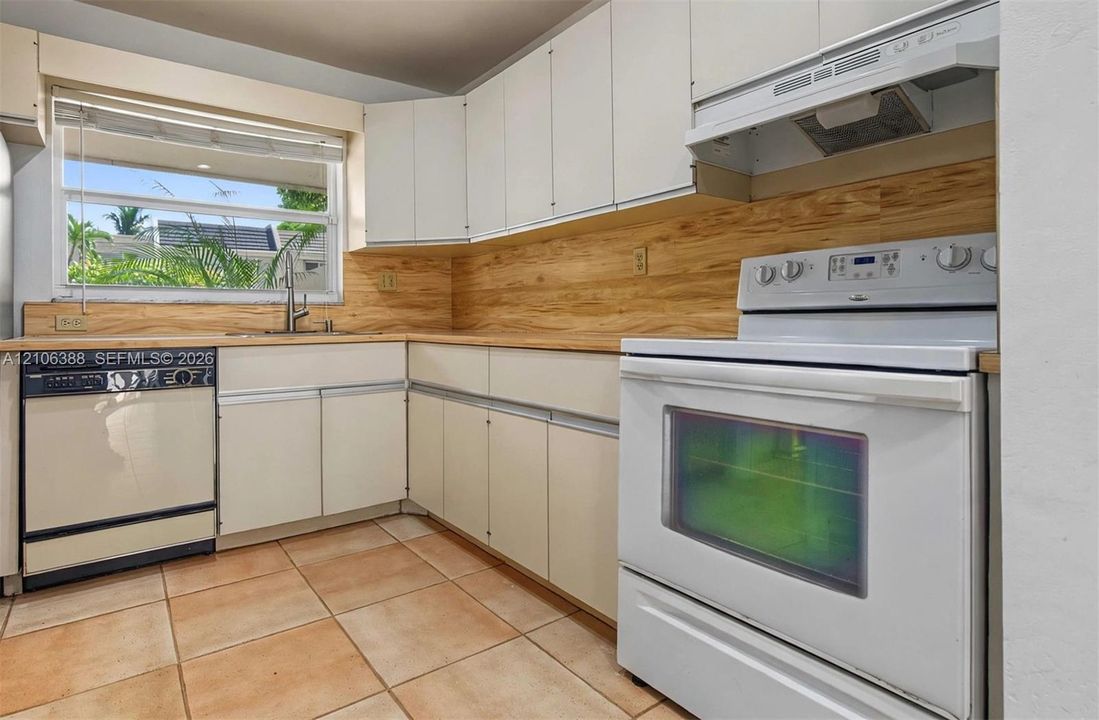 Kitchen featuring white cabinetry, light wood-tone backsplash, integrated range hood, ceramic tile flooring, and a stainless steel kitchen faucet