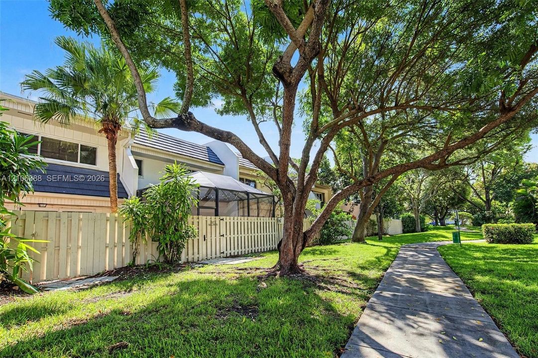 Exterior featuring a fenced-in patio with a screen enclosure, concrete walkway, mature trees, and landscaping