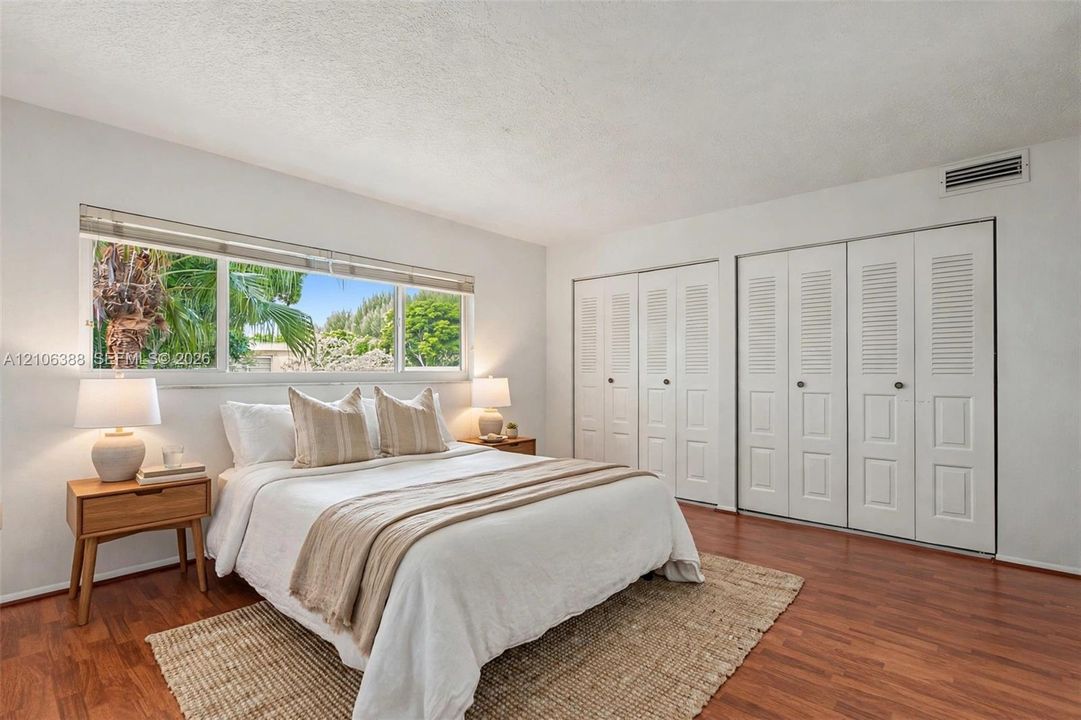 Horizontal sliding window with exterior greenery, wood-finish flooring, and double-door louvered closets