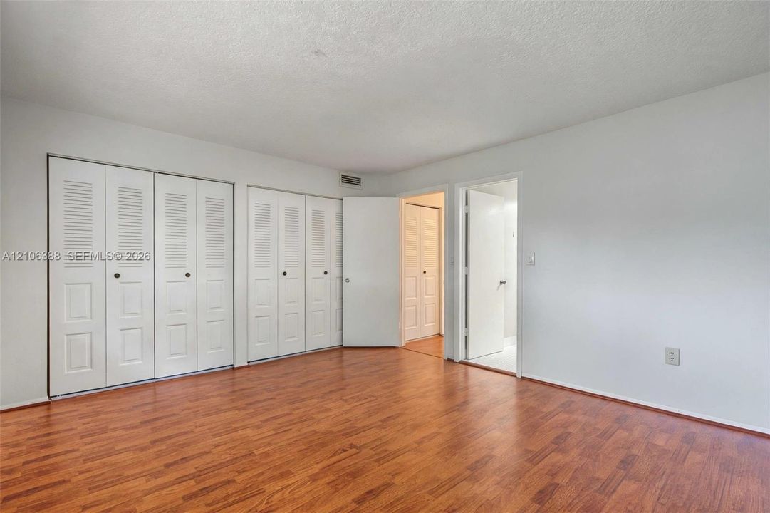 Room featuring wood-finish flooring, multiple sets of white bi-fold closet doors, and solid-core interior doors