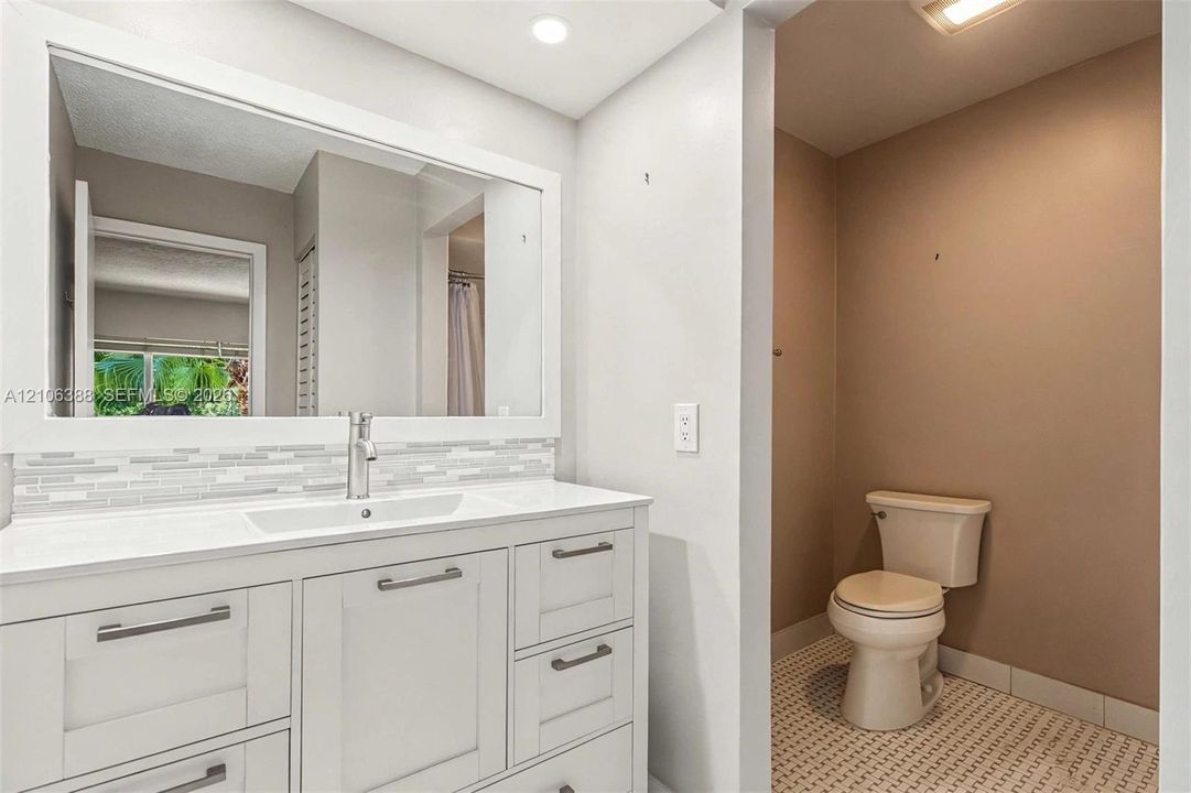 White shaker-style cabinetry with a smooth surface countertop, rectangular integrated basin, decorative glass tile backsplash, and oversized wall-mounted mirror
