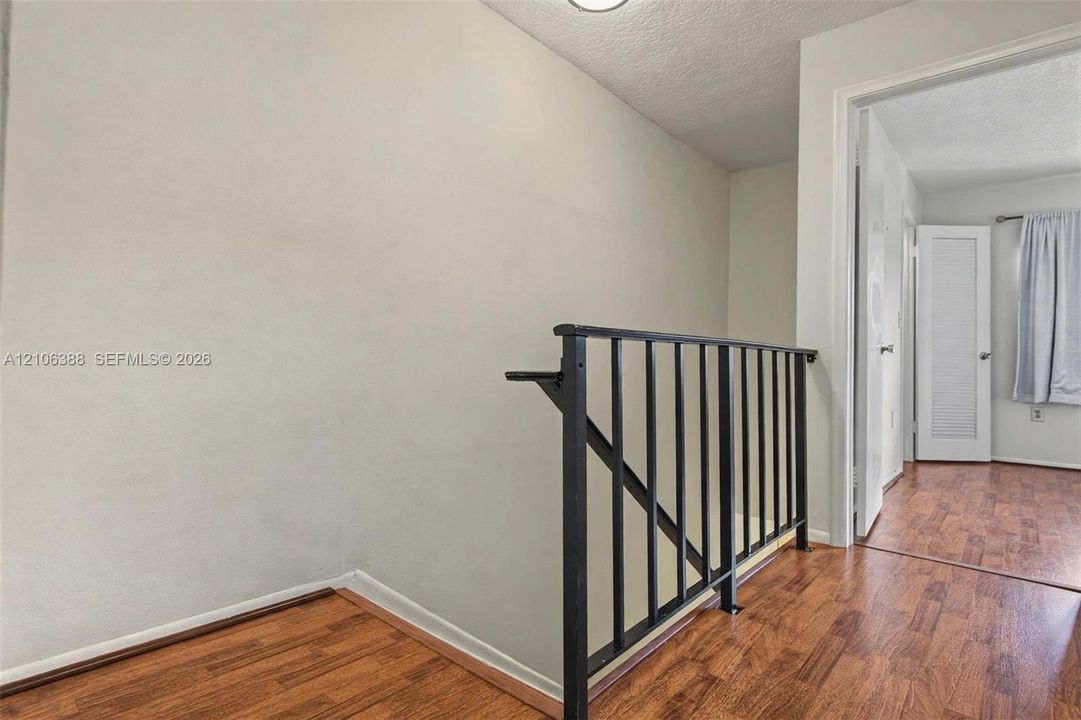 Wood-finish flooring featuring a black metal balustrade and a louvered panel door