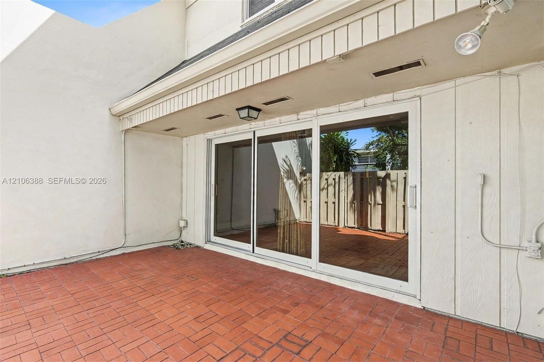 Private patio featuring red brick paving, a three-panel sliding glass door, and a covered entryway with integrated lighting
