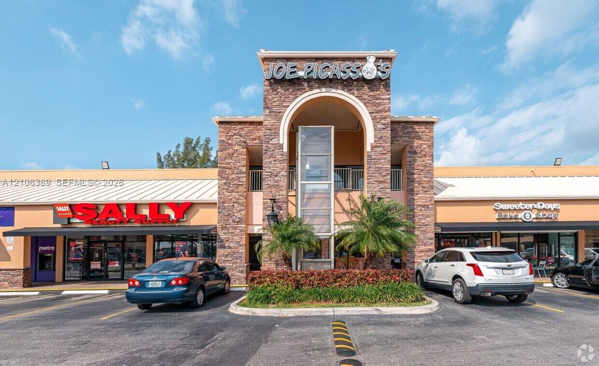 Commercial storefront featuring a decorative stone facade, an arched architectural entryway, glass-enclosed stairwell, and a paved parking lot