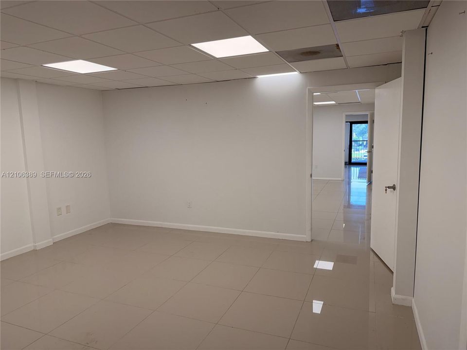 Interior room featuring large-format neutral floor tile, a drop ceiling with recessed panel lighting, and solid white wall finishes