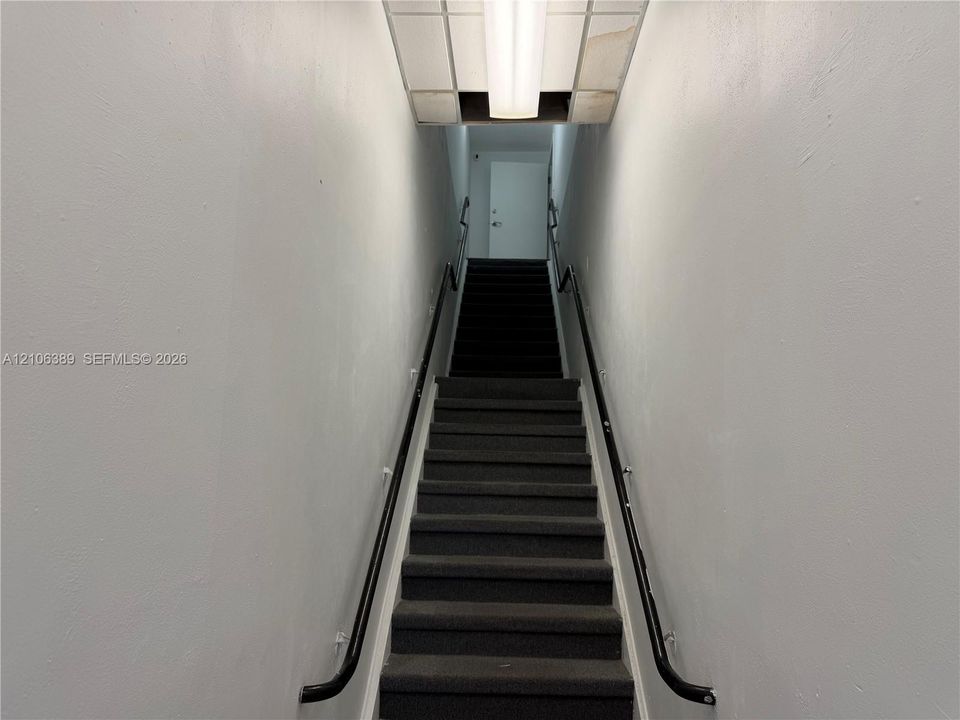 Staircase featuring dark carpeting, dual black handrails, and a recessed ceiling light fixture