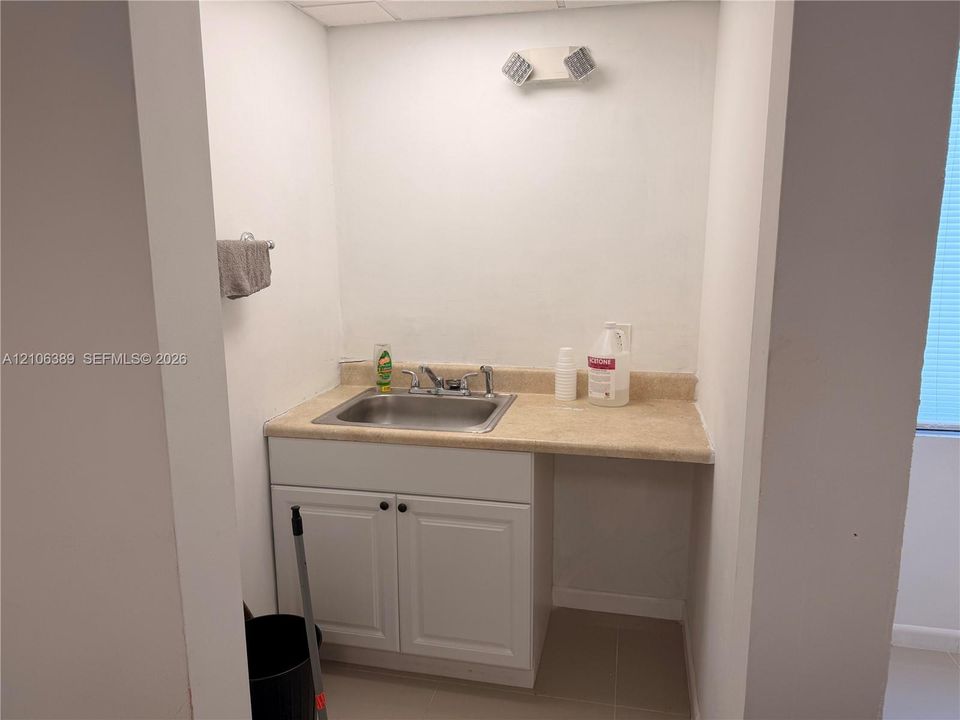 Utility area featuring a white shaker-style cabinet, a textured stone-finish countertop, an integrated stainless steel sink, and a dual-handle faucet